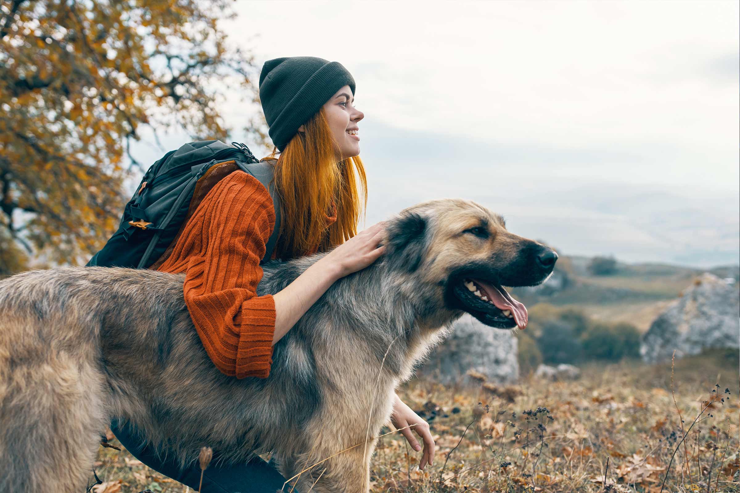 Frau streichelt Hund in der Natur mit Rucksack und Mütze
