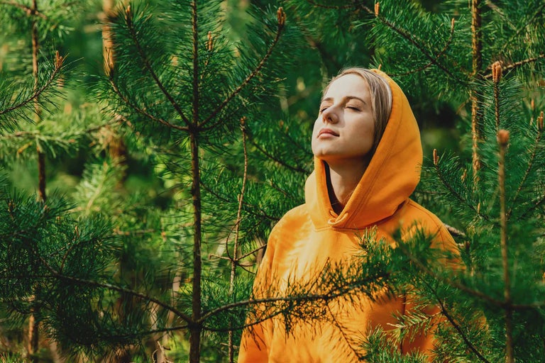 Femme aux yeux fermés dans une pinède avec un sweat à capuche