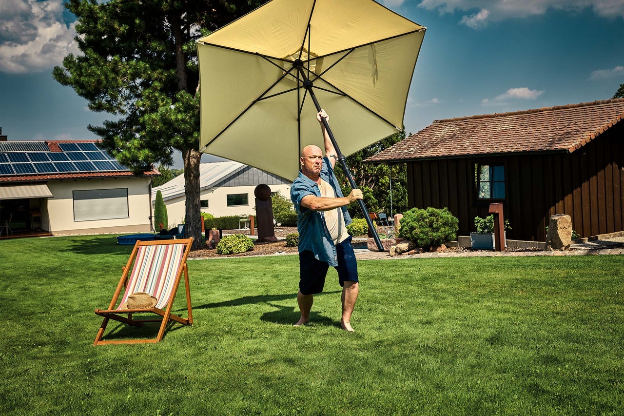 Mann hievt Sonnenschirm in Garten mit Liegestuhl