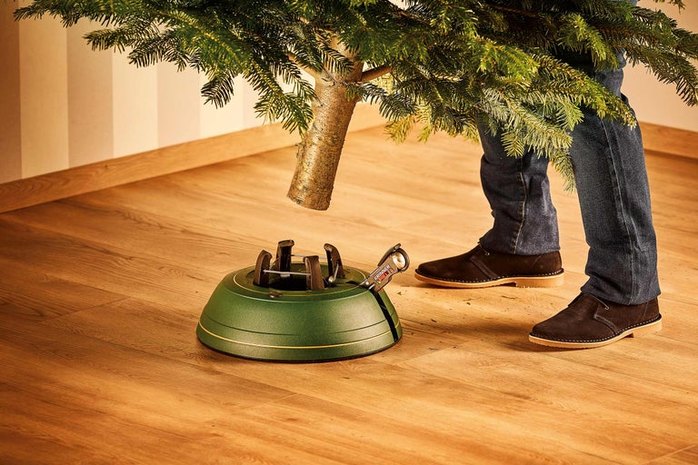 Eine Person stellt einen Weihnachtsbaum in einen grünen Christbaumständer.