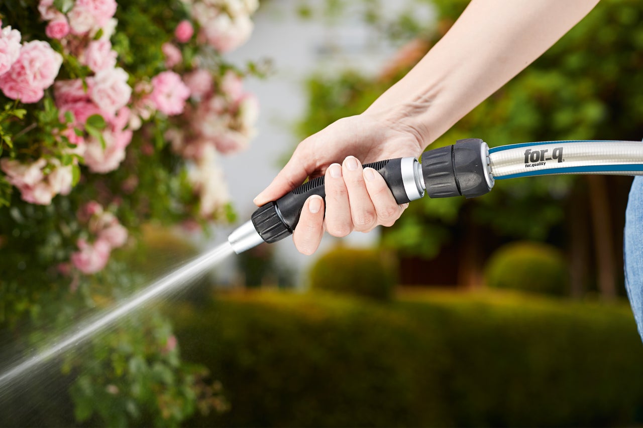 Eine Person hält einen Gartenschlauch mit Sprühdüse in der Hand und bewässert Pflanzen.
