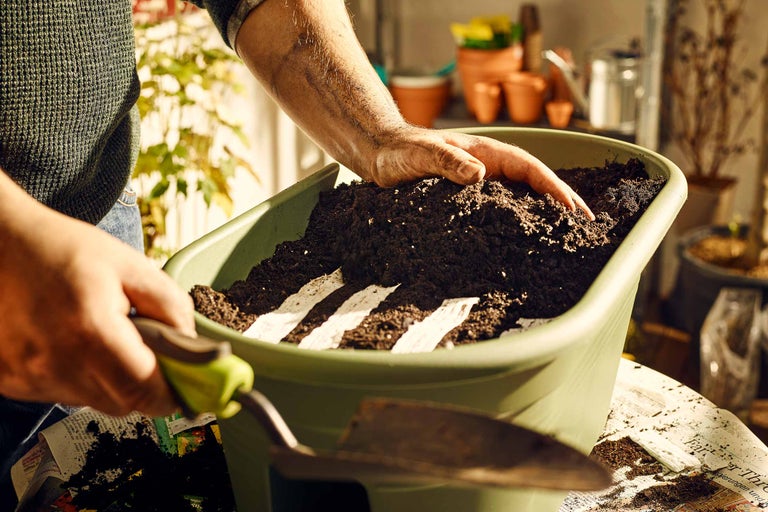 Une personne remplit un bac à plantes avec de la terre et des toiles de semis.