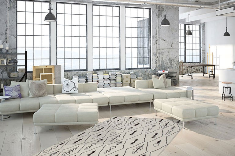 Salon spacieux avec canapé modulable, tapis et grandes fenêtres de style loft.