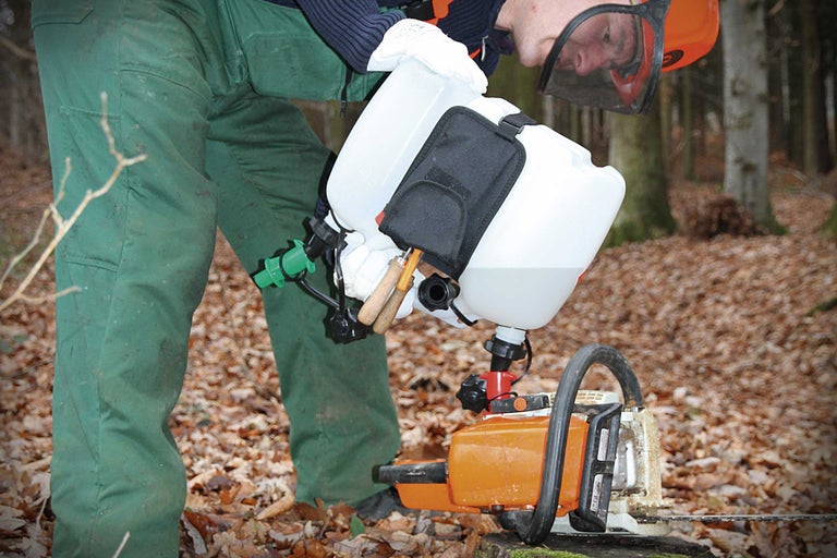 Eine Person befüllt eine Kettensäge mit einem Kanister mit Einfüllsystem.
