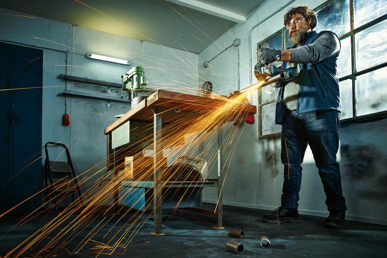 Handwerker beim Schneiden von Metall mit einem Winkelschleifer in einer Werkstatt, Funken fliegen.