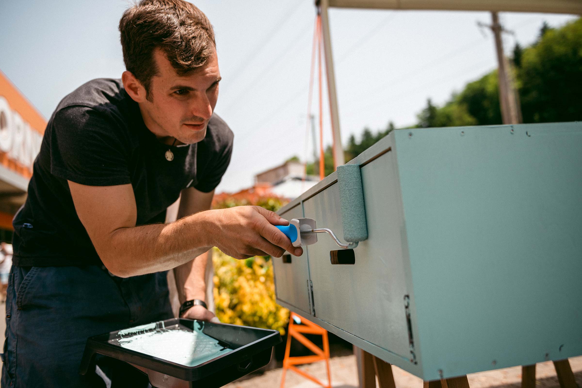 Homme peignant une armoire avec un rouleau à peinture et un bac à peinture