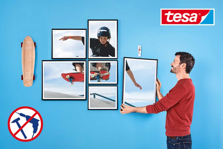 Décoration murale avec les solutions adhésives Tesa: cadres photo, skateboard et logo Tesa sur un mur bleu. Symbole: Ne pas utiliser de perceuse ou de marteau.