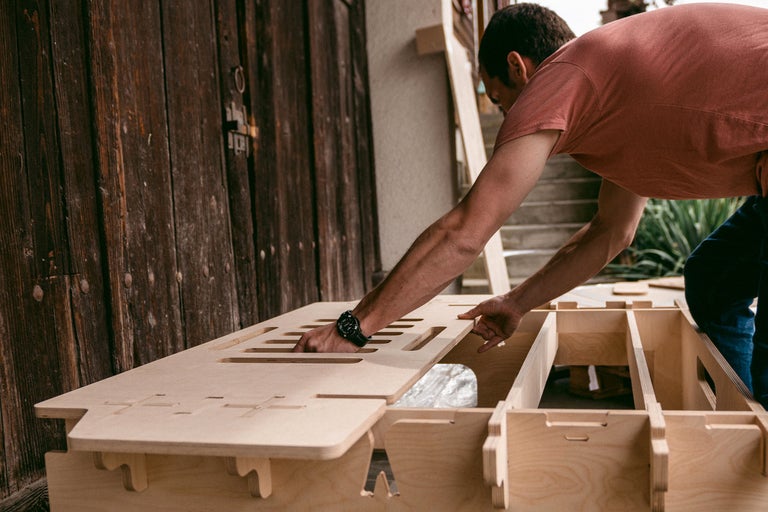Mann montiert ein Möbelstück aus Holz im Freien.