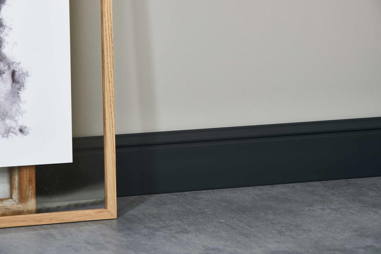 Detailaufnahme einer dunkel lackierten Fussleiste an einer Wand