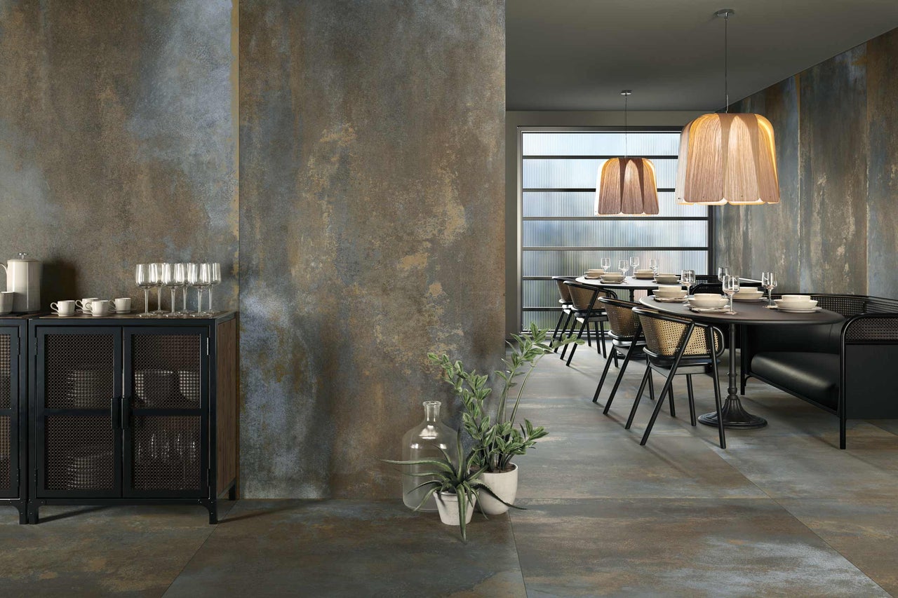 Intérieur avec tables, chaises et un buffet devant un mur à l'aspect rouille.