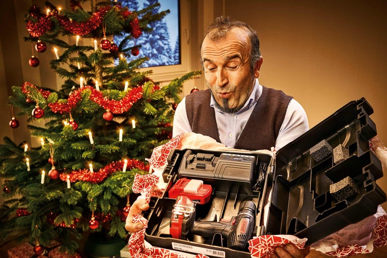 Un homme ouvre avec surprise une boîte à outils à côté d'un arbre de Noël décoré