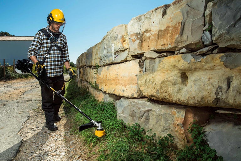 Homme avec casque de sécurité et coupe-bordure devant un mur de pierre