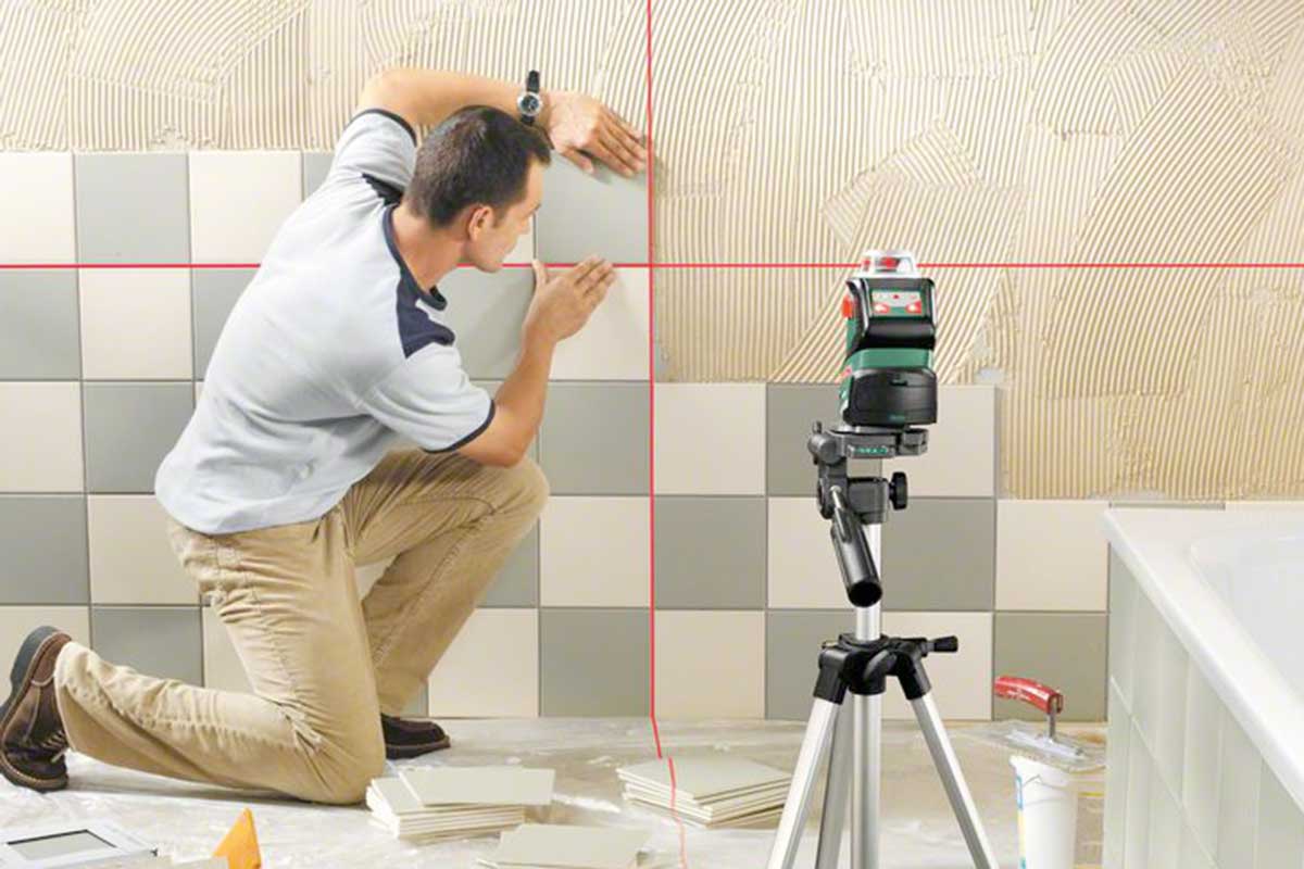 Artisan pose des carreaux avec un laser lignes croisées dans la salle de bain