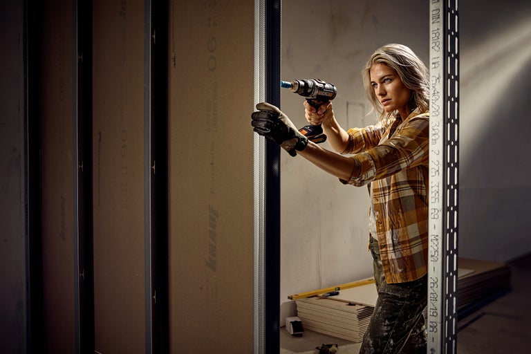 Frau befestigt eine Gipskartonplatte mit einem Akkubohrer an einem Metallständerwerk von Knauf.