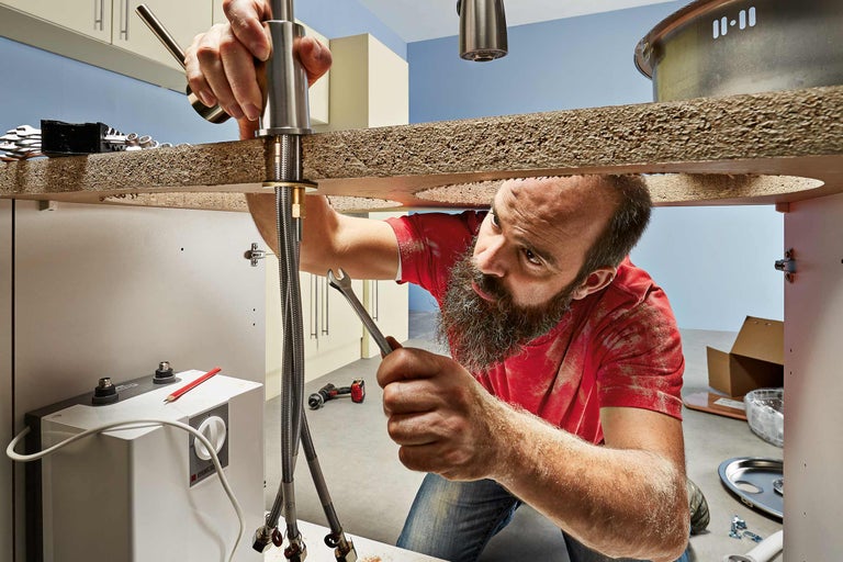 Ein Installateur montiert eine Armatur mit einem Schraubenschlüssel in einer Küche.