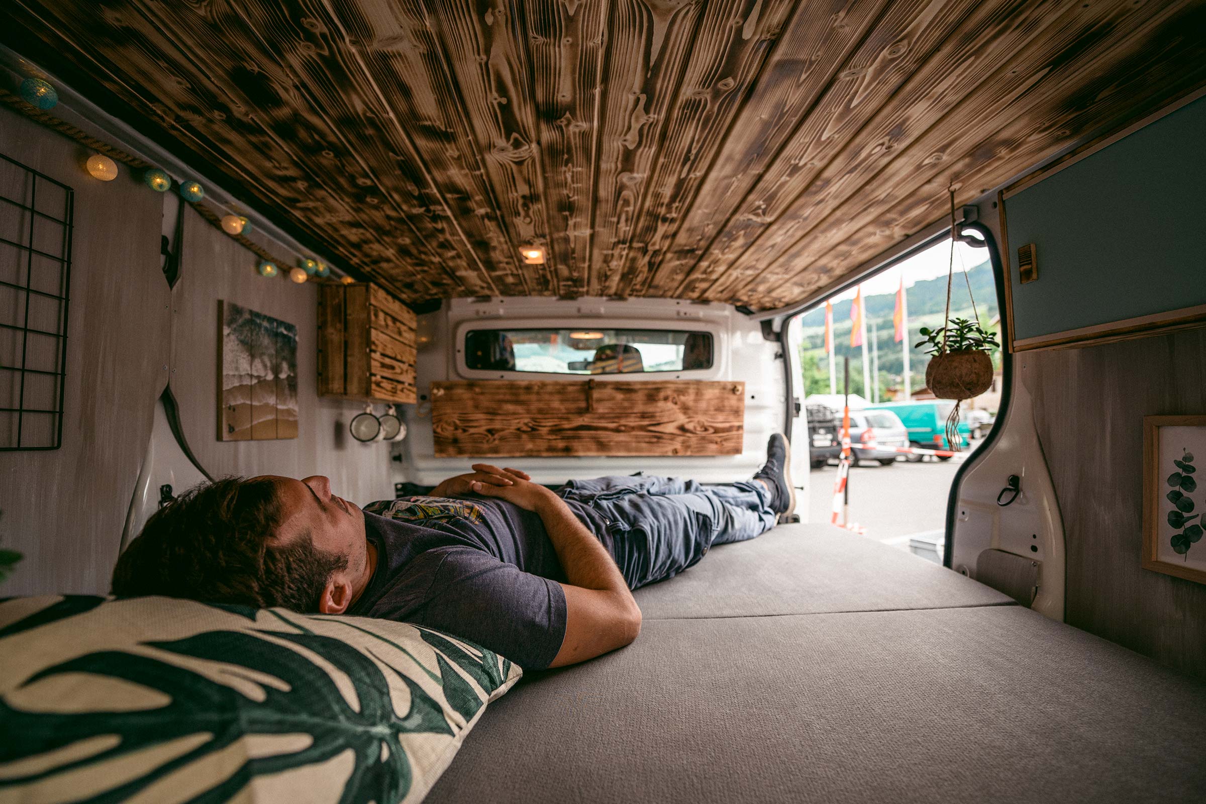 Intérieur d'une camionnette aménagée avec des lambris en bois et une personne allongée sur un lit