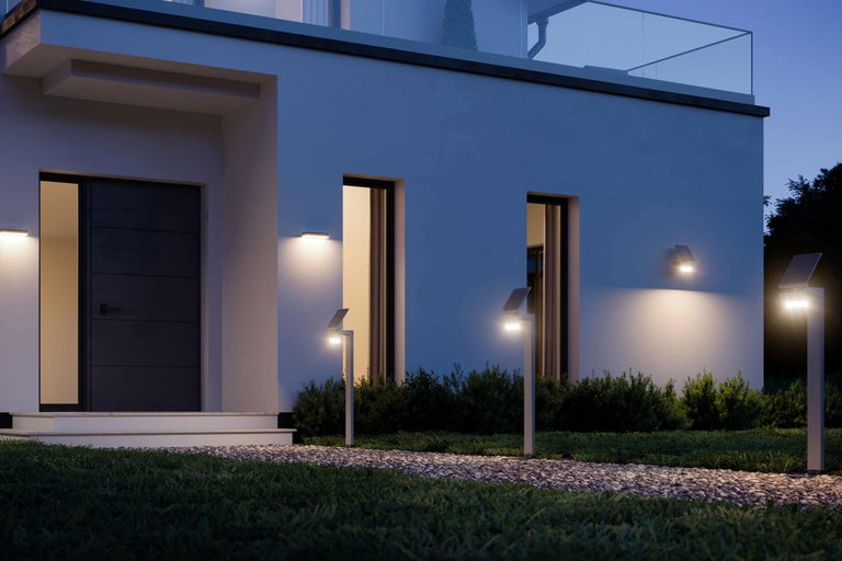 Aussenansicht eines Hauses mit Solarleuchten entlang eines Kieswegs und Wandleuchten neben der Haustür und Fenstern