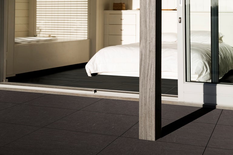 Terrasse avec des carreaux foncés, vue sur une chambre avec lit et salle de bain