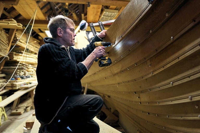 Ein Mann bohrt eine Bootswand mit einer Bohrmaschine in einer Werkstatt.