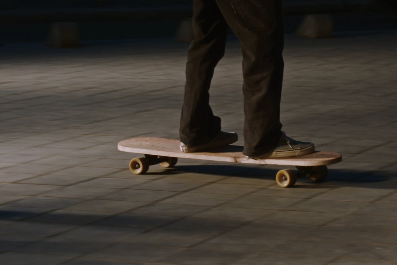 Eine Person auf einem Skateboard aus Holz auf einem gepflasterten Boden.