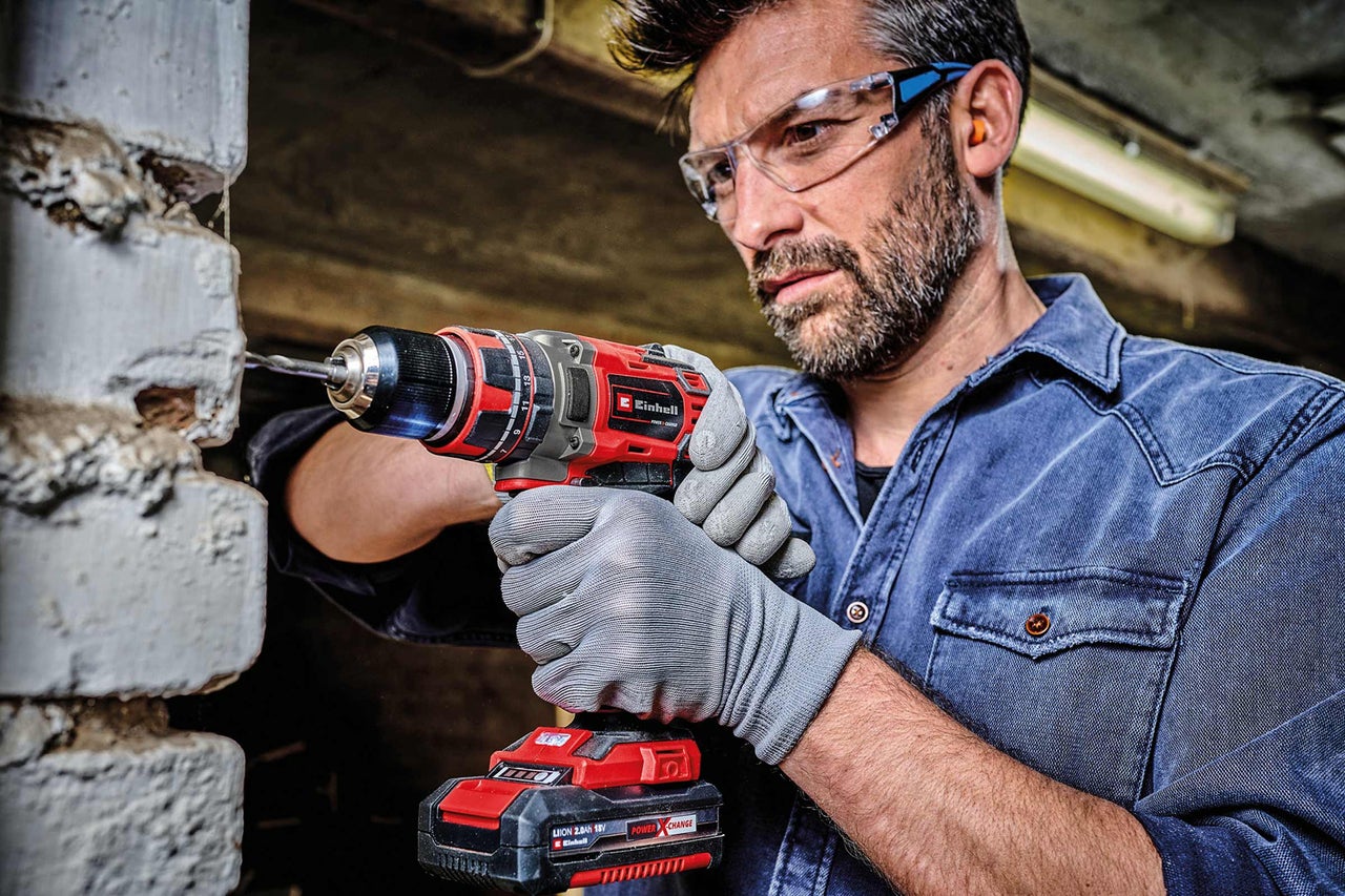 Mann bohrt mit Akku-Bohrschrauber in eine Ziegelwand. Einhell Logo.