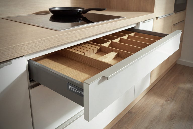 Tiroir de cuisine ouvert avec range couverts en bois dans une cuisine moderne équipée d une plaque à induction et d une poêle.