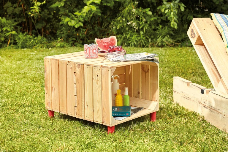 Scène de jardin avec une caisse en bois servant de table, décorée de fruits et de boissons