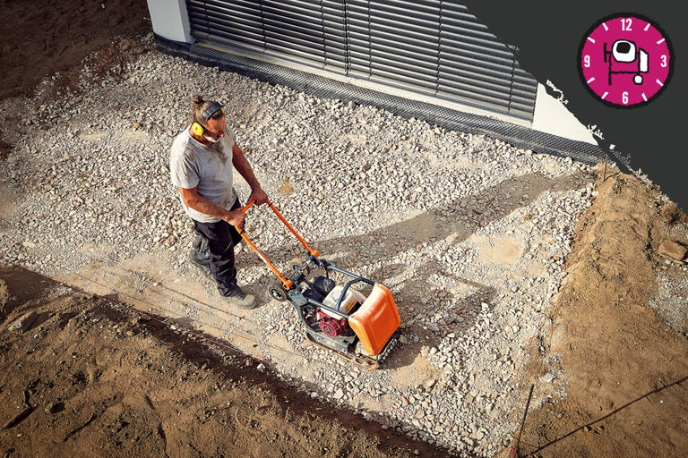 Ein Mann verdichtet mit einer Vibrationsplatte Kies auf einer Baustelle.
