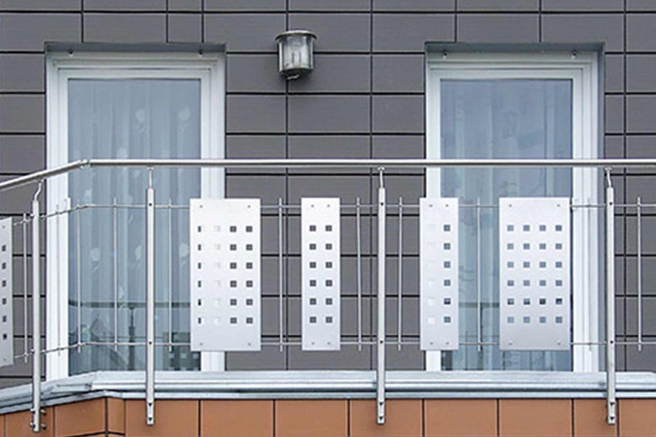 Balkon mit Geländer aus Metall und perforierten Paneelen vor einer Fassade mit zwei Fenstern.