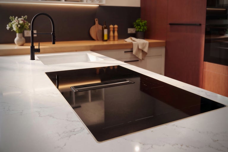 Îlot de cuisine moderne avec table de cuisson à induction et hotte intégrée, plan de travail blanc effet marbre et robinetterie noire.