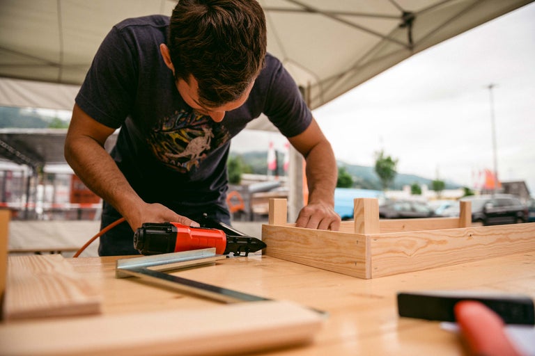 Mann arbeitet mit einem Druckluftnagler an einem Holzrahmen.