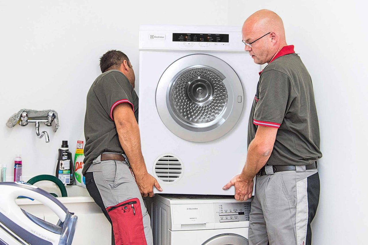 Zwei Handwerker installieren einen Electrolux Trockner auf einer Waschmaschine
