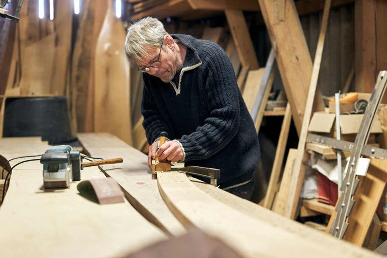 Mann arbeitet mit einem Hobel an einem Holzstück in einer Werkstatt.