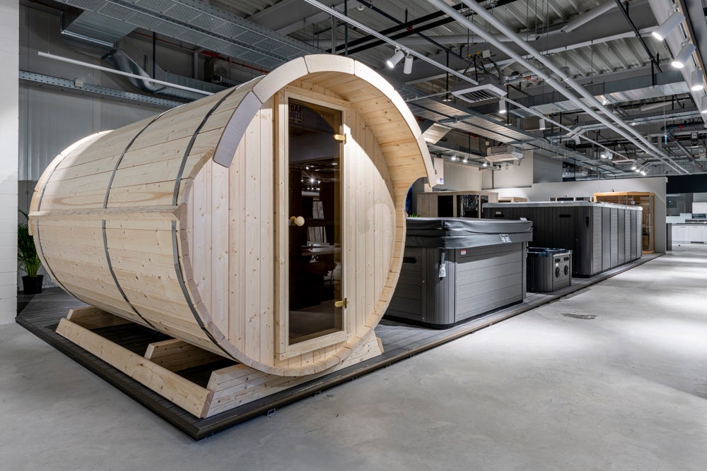 Fasssauna aus Holz mit Glastür neben mehreren Whirlpools