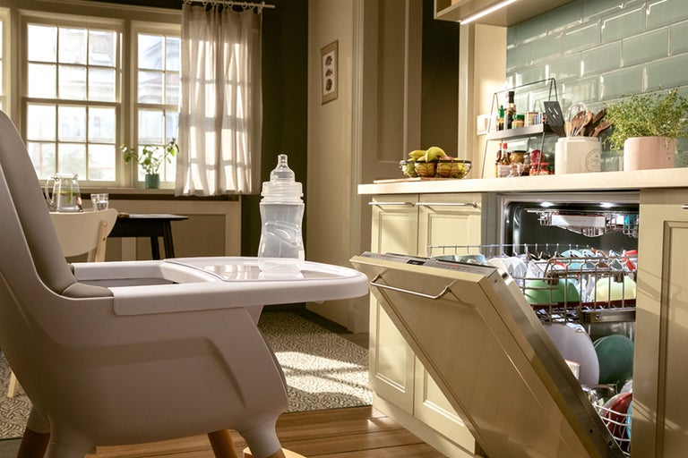 Scène de cuisine avec une chaise haute pour enfant, un biberon et un lave-vaisselle avec de la vaisselle