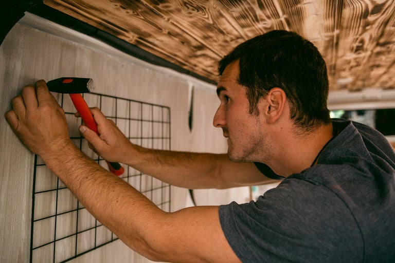 Ein Mann befestigt ein Gitter mit einem Hammer an einer Wand.