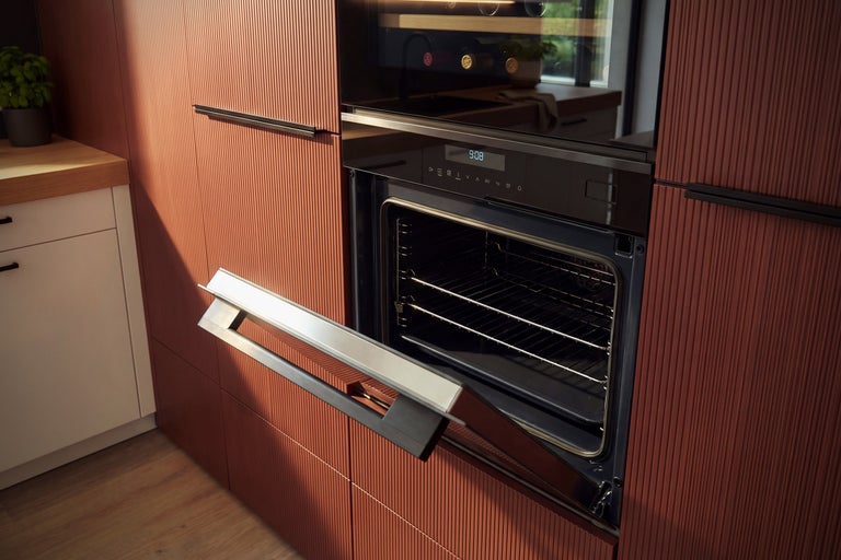 Four moderne avec porte ouverte dans une cuisine élégante avec façades rainurées et plan de travail en bois.