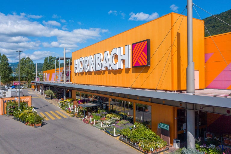 Vue extérieure d'un magasin de bricolage Hornbach avec des plantes devant l'entrée.