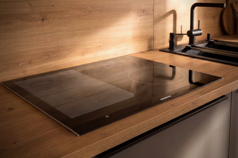 Siemens Induktionskochfeld mit FlexInduction in einer modernen Holzküchenzeile mit dunkler Spüle.