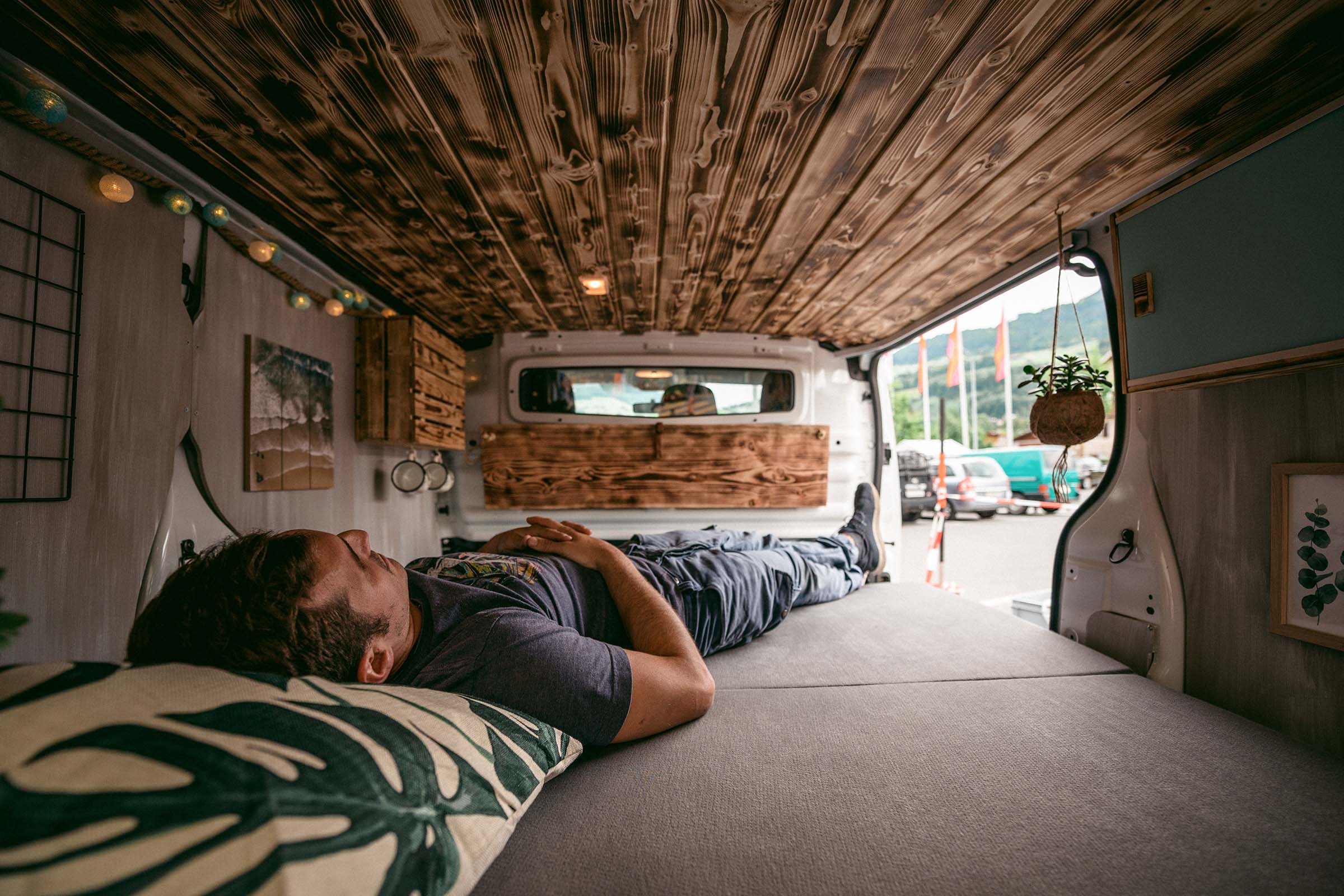 Intérieur d'une camionnette transformée avec un plafond en bois et une personne allongée sur un lit