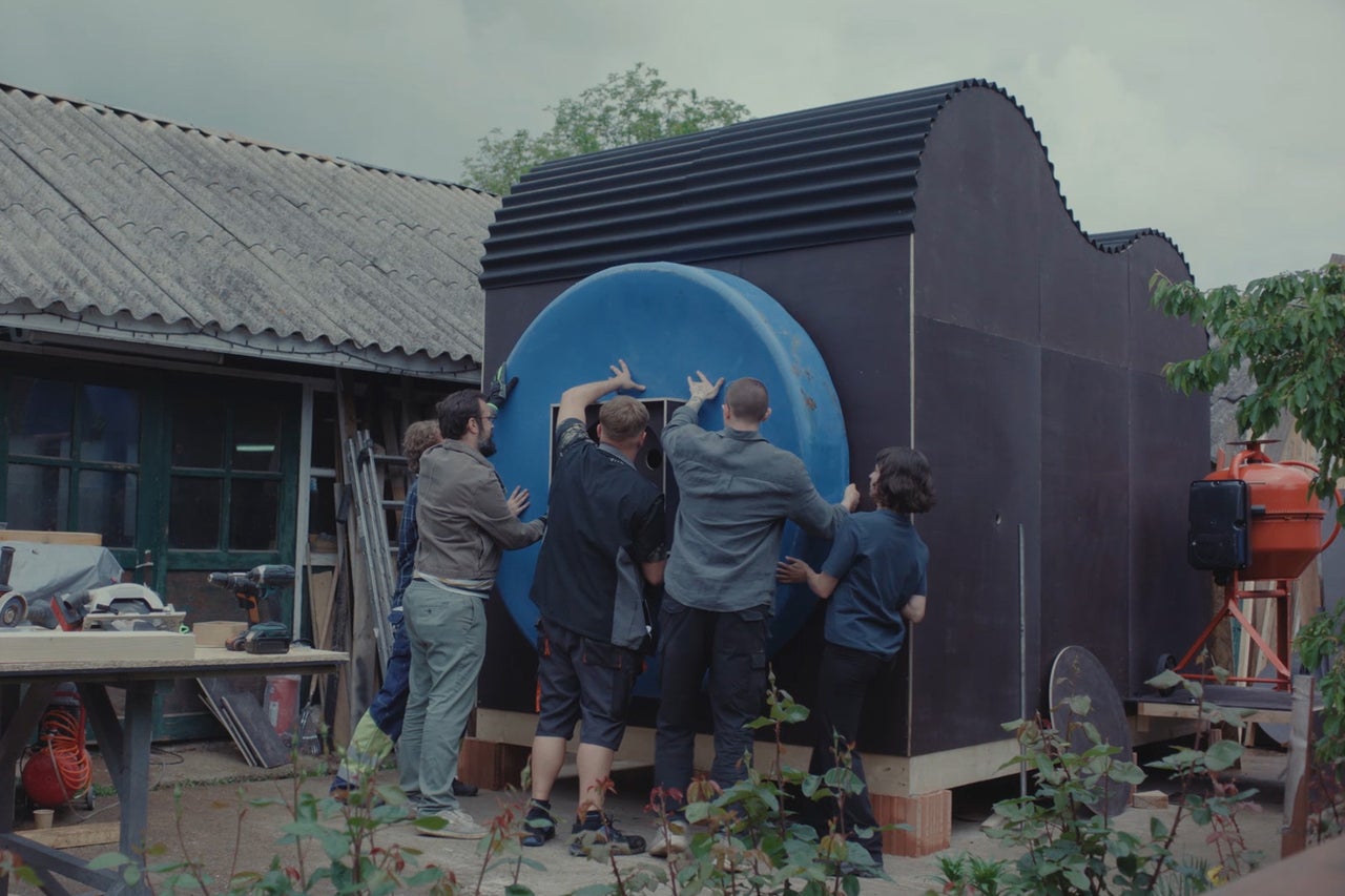 Eine Gruppe von Personen arbeitet gemeinsam am Aufbau einer modernen schwarzen Gartenhütte mit einem grossen runden blauen Element.