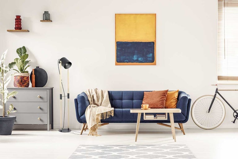 Wohnzimmer mit blauem Sofa, Holztisch, Kommode und Stehlampe