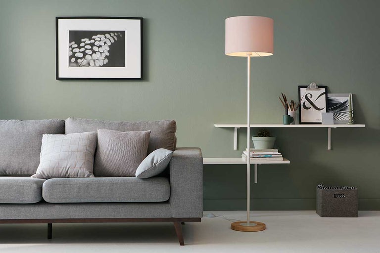 Wohnzimmer mit grauem Sofa, Stehlampe und Wandregal.
