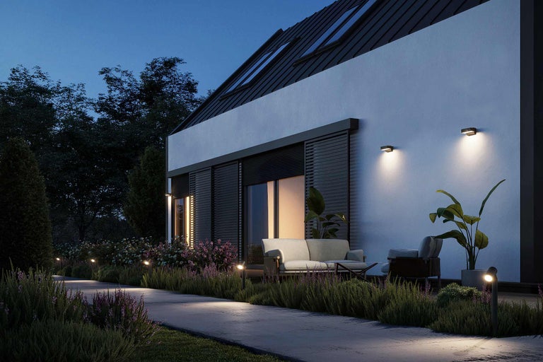 Aussenansicht eines modernen Hauses mit Gartenbeleuchtung und Gartenmöbeln in der Abenddämmerung.