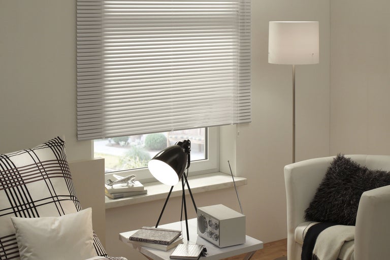 Salon avec store vénitien, lampe, radio et fauteuil pour une ambiance chaleureuse