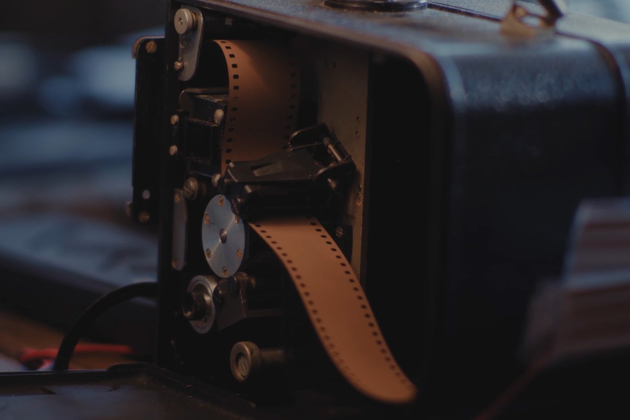 Historischer Filmprojektor mit eingelegtem Filmstreifen im Inneren des Gehäuses.