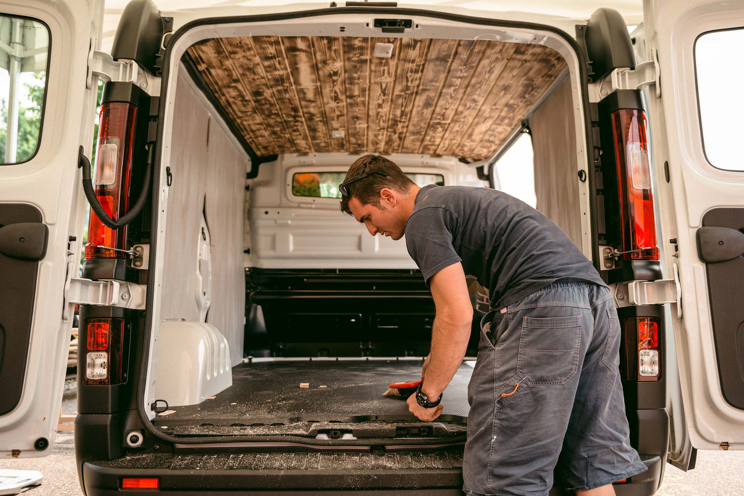 Intérieur d'une camionnette avec revêtement en bois au plafond et une personne nettoyant le sol