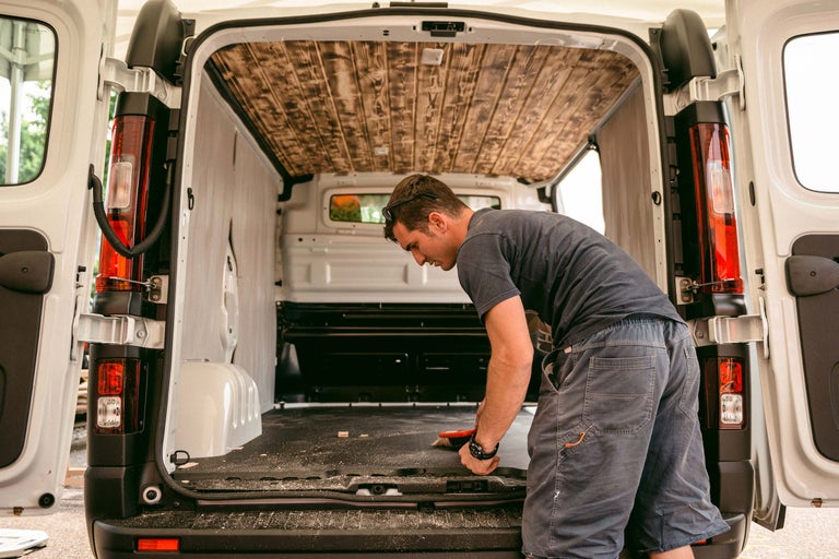 Innenansicht eines Transporters mit Holzverkleidung an der Decke und einer Person, die den Boden reinigt