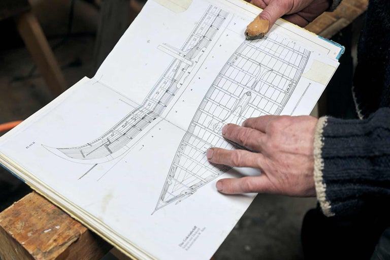 Hand hält geöffnetes Buch mit Planzeichnungen für ein Boot
