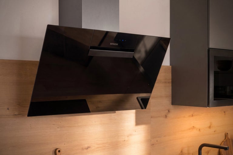 Moderne Siemens Dunstabzugshaube mit geneigtem Glaspaneel montiert an einer Küchenwand mit Holzoptik.